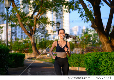 Asian sportswoman with earbuds running in park 142775851