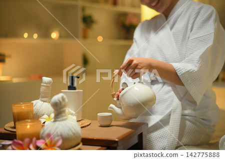 Woman pouring herbal tea in spa setting with warm light and calm wellness mood Woman pouring herbal tea in spa setting with warm light and calm wellness mood 142775888