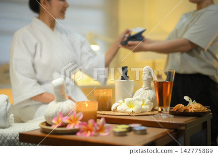 Spa still life with herbal compress and welcome drink with woman paying with card in background Spa still life with herbal compress and welcome drink with woman paying with card in background 142775889