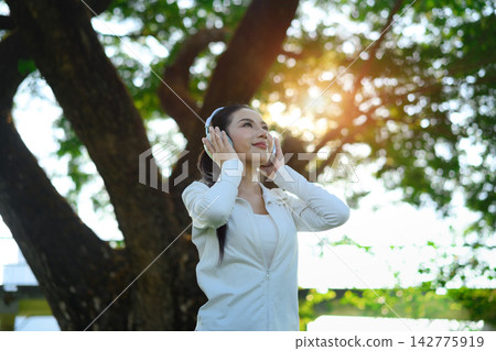 Sporty woman athlete listening to music in a green park environment Sporty woman athlete listening to music in a green park environment 142775919