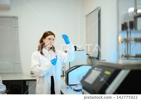 Female Scientist Examining Sample Vial in Modern Research Laboratory with Scientific Equipment Female Scientist Examining Sample Vial in Modern Research Laboratory with Scientific Equipment 142775922