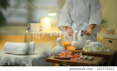 Cropped shot woman hand preparing spa tools with candles herbal compress and warm relaxing atmosphere Cropped shot woman hand preparing spa tools with candles herbal compress and warm relaxing atmosphere 142775923