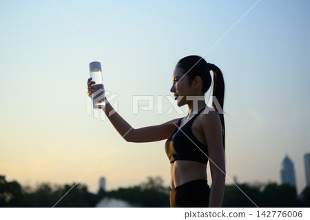 Woman drinks water after workout by lake at sunset Woman drinks water after workout by lake at sunset 142776006