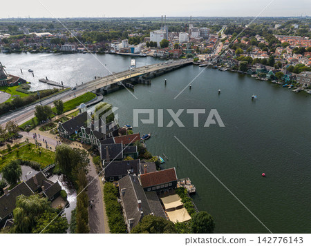 High angle wide horizontal aerial drone photograph of Zaanse Schans village, Julianabrug bridge over Zaan river, green wooden houses, and industrial Zaandijk in Zaandam, North Holland, Netherlands High angle wide horizontal aerial drone photograph of Zaanse Schans village, Julianabrug bridge over Zaan river, green wooden houses, and industrial Zaandijk in Zaandam, North Holland, Netherlands 142776143