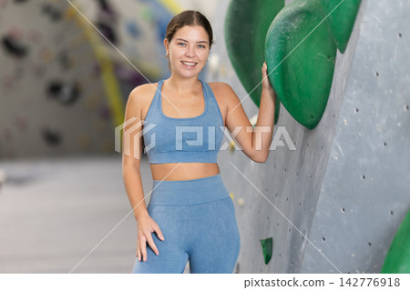 Girl posing near climbing wall at bouldering gym after workout, feeling accomplished and energized Girl posing near climbing wall at bouldering gym after workout, feeling accomplished and energized 142776918