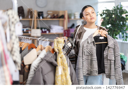 Adult woman chooses coat in clothing store Adult woman chooses coat in clothing store 142776947