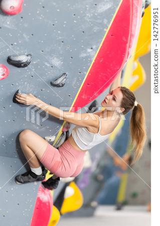 Girl climbs artificial wall bouldering, working out in gym Girl climbs artificial wall bouldering, working out in gym 142776951