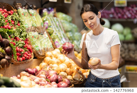 Girl client near vegetable stand in store choose onion Girl client near vegetable stand in store choose onion 142776968