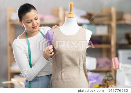 Young sewing woman professional measuring new dress at mannequin at atelier Young sewing woman professional measuring new dress at mannequin at atelier 142776980