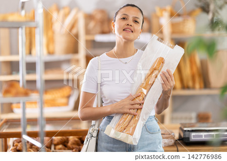 Middle-aged woman holding baguettes in paper bag in bakery Middle-aged woman holding baguettes in paper bag in bakery 142776986