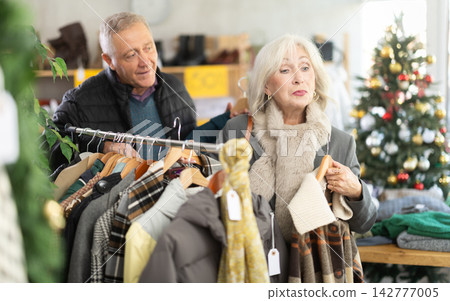 Positive mature man and woman choosing coat or jacket in clothing store Positive mature man and woman choosing coat or jacket in clothing store 142777005
