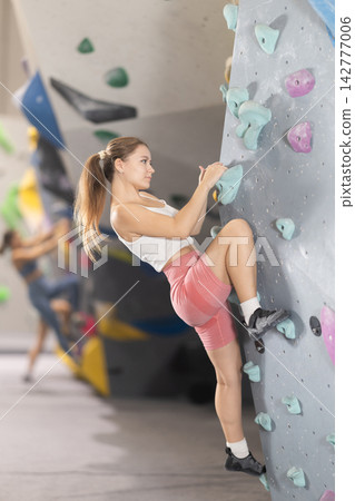 Girl climbs artificial wall bouldering, working out in gym Girl climbs artificial wall bouldering, working out in gym 142777006