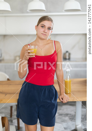 Happy teenage girl drinking juice or smoothie in kitchen at home Happy teenage girl drinking juice or smoothie in kitchen at home 142777041