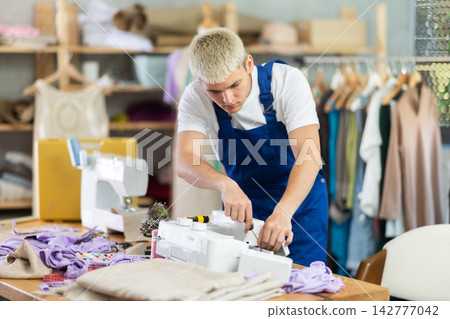 Repairman repairing sewing machine in workshop Repairman repairing sewing machine in workshop 142777042