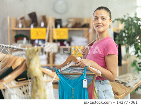 Positive joyful woman looking for fashionable clothes in clothing boutique Positive joyful woman looking for fashionable clothes in clothing boutique 142777061