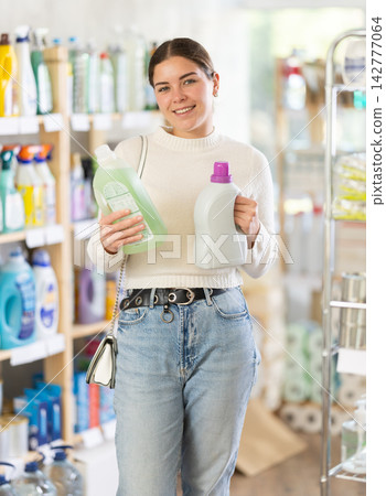 Girl housewife in household store examines package, chooses liquid detergent Girl housewife in household store examines package, chooses liquid detergent 142777064