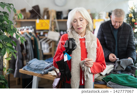 mature woman chooses gloves against the background of a Christmas tree mature woman chooses gloves against the background of a Christmas tree 142777067