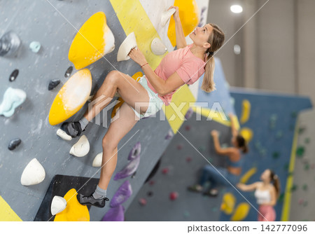 Woman doing difficult wall climb in climbing gym Woman doing difficult wall climb in climbing gym 142777096