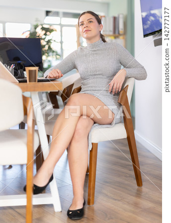 Young woman sitting at desk and drinking coffee in office 142777177