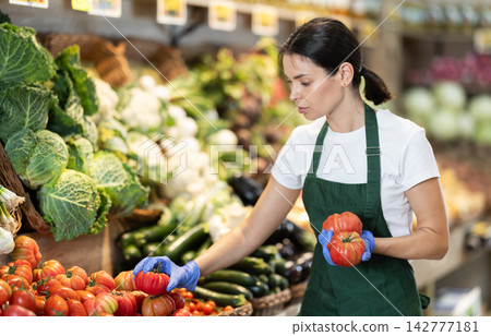 Supermarket employee carefully places ripe tomatoes on shelves of grocery supermarket Supermarket employee carefully places ripe tomatoes on shelves of grocery supermarket 142777181