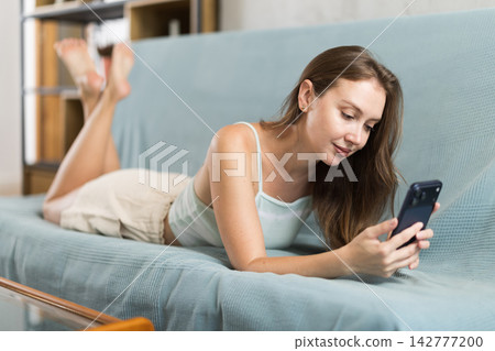 Adult woman scrolling smartphone on sofa Adult woman scrolling smartphone on sofa 142777200
