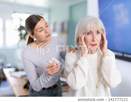Elderly businesswoman suffers from a headache. Colleague offers her headache pills. Elderly businesswoman suffers from a headache. Colleague offers her headache pills. 142777221