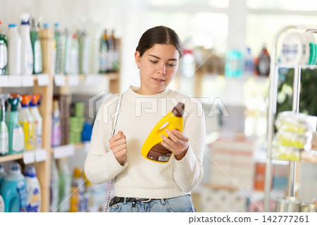 Girl housewife in household store examines and chooses polishing agent for wooden furniture, parquet Girl housewife in household store examines and chooses polishing agent for wooden furniture, parquet 142777261
