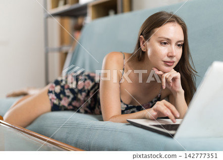 Woman freelancer working on laptop in living room and solving work issues Woman freelancer working on laptop in living room and solving work issues 142777351