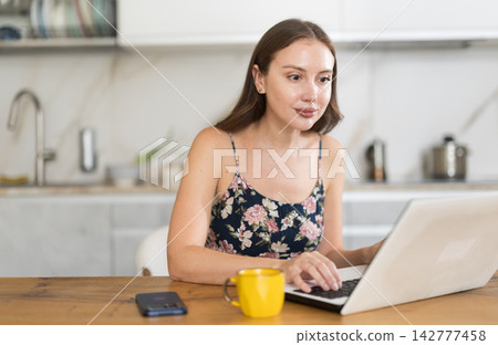 Woman working in the kitchen on laptop and drinking delicious coffee Woman working in the kitchen on laptop and drinking delicious coffee 142777458