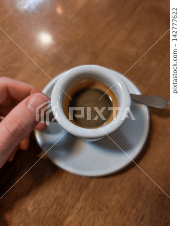 Hand holding espresso cup on wooden table in brandys nad labem cafe Hand holding espresso cup on wooden table in brandys nad labem cafe 142777622