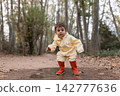 Toddler playing in puddle wearing raincoat and boots 142777636