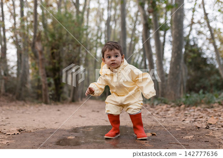 Toddler playing in puddle wearing raincoat and boots Toddler playing in puddle wearing raincoat and boots 142777636