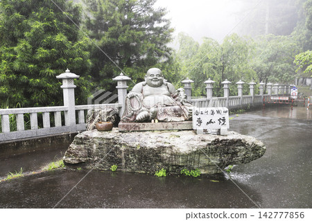 朝聖路線上的第十二座寺廟:丸山正壽院正山寺。布袋和尚(幸福與好運之神)在雨中迎接遊客。 朝聖路線上的第十二座寺廟:丸山正壽院正山寺。布袋和尚(幸福與好運之神)在雨中迎接遊客。 142777856