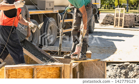 Concrete is being poured into forms to create a solid foundation at a construction site. The workers are using a concrete pump and molds Concrete is being poured into forms to create a solid foundation at a construction site. The workers are using a concrete pump and molds 142779129