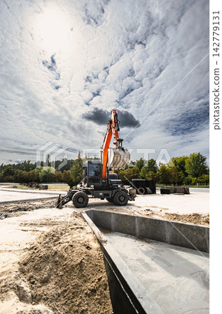 Excavator operates at a rental site, moving dirt for landscaping project. The machine digs and shapes the ground in preparation for further work 142779131
