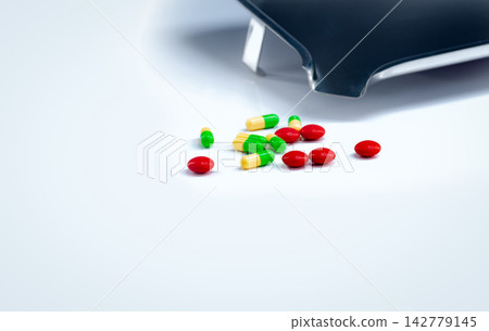 Red tablets and green-yellow capsules pills with drug tray on white table. Pharmaceutical industry. Vitamins and supplements. Pharmaceutics concept. Pharmacy products. Healthcare and medication. 142779145