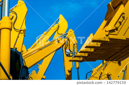 Yellow backhoe with hydraulic piston arm against clear blue sky. Heavy machine for excavation in construction site. Hydraulic machinery. Huge bulldozer. Heavy industry Yellow backhoe with hydraulic piston arm against clear blue sky. Heavy machine for excavation in construction site. Hydraulic machinery. Huge bulldozer. Heavy industry 142779150