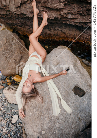 Stunning blonde woman wearing white swimwear lying against rocky coastal background enjoying tranquility Stunning blonde woman wearing white swimwear lying against rocky coastal background enjoying tranquility 142779228