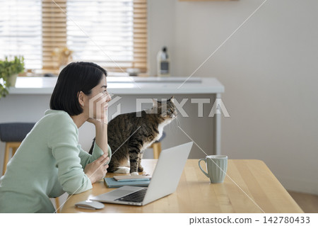 Life with a cat: A young woman resting her chin on her hand in front of her laptop, and her cat. Life with a cat: A young woman resting her chin on her hand in front of her laptop, and her cat. 142780433