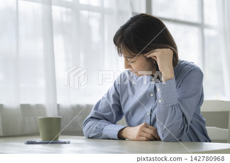 A woman in her late 40s holding her temples. A woman in her late 40s holding her temples. 142780968