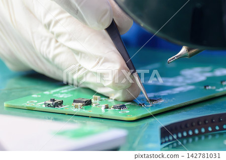 Skilled operator soldering an electronic circuit board while wearing protective rubber gloves Skilled operator soldering an electronic circuit board while wearing protective rubber gloves 142781031