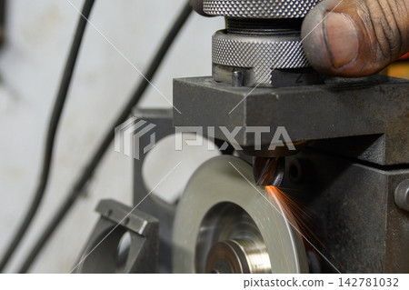 Skilled operator manually regrinding a flat nose end mill on a tool regrinding machine Skilled operator manually regrinding a flat nose end mill on a tool regrinding machine 142781032