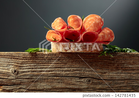 Sandwich with thin slices salami and rosemary on a wooden table. Sandwich with thin slices salami and rosemary on a wooden table. 142781435