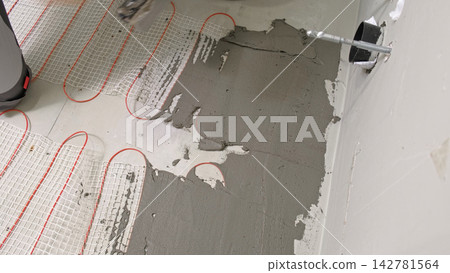 Worker installing electric underfloor heating system mat. Underf 142781564