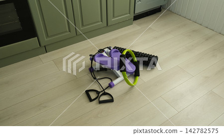 Mini stepper machine with pilates ring and foam roller on floor at home. Domestic fitness equipment set. Compact workout gear for indoor cardio and strength training. Home gym and weight loss concept. Mini stepper machine with pilates ring and foam roller on floor at home. Domestic fitness equipment set. Compact workout gear for indoor cardio and strength training. Home gym and weight loss concept. 142782575