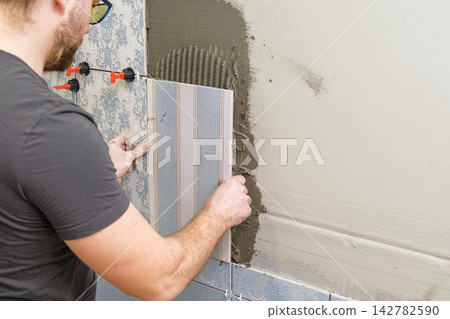 Professional tiler installing ceramic wall tiles with adhesive m Professional tiler installing ceramic wall tiles with adhesive m 142782590