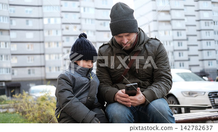 Caring father showing smartphone screen to little son outdoors. Dad and boy sitting near house, using mobile phone together. Digital Parenting, Screen Time Management. Parent and child with smartphone Caring father showing smartphone screen to little son outdoors. Dad and boy sitting near house, using mobile phone together. Digital Parenting, Screen Time Management. Parent and child with smartphone 142782637