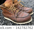 A photograph of leather work boots placed on gravel. 142782762