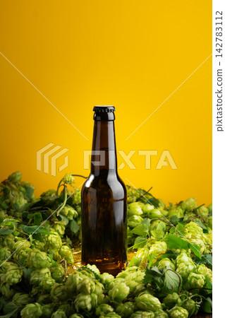 Amber glass bottle of craft beer surrounded by fresh green hops flowers with yellow background Amber glass bottle of craft beer surrounded by fresh green hops flowers with yellow background 142783112