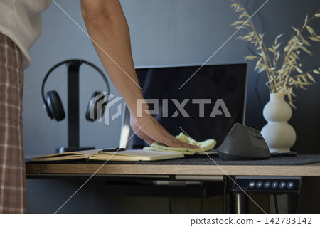 Person wiping wooden desk with cloth beside monitor, mouse, headphones and notebook Person wiping wooden desk with cloth beside monitor, mouse, headphones and notebook 142783142